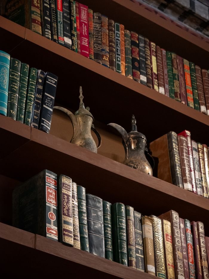 Ornate old teapots and various books on a wooden shelf.